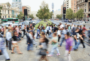 Cena urbana com fluxo intenso de pessoas atravessando a rua, retratando a correria do cotidiano nas grandes cidades.